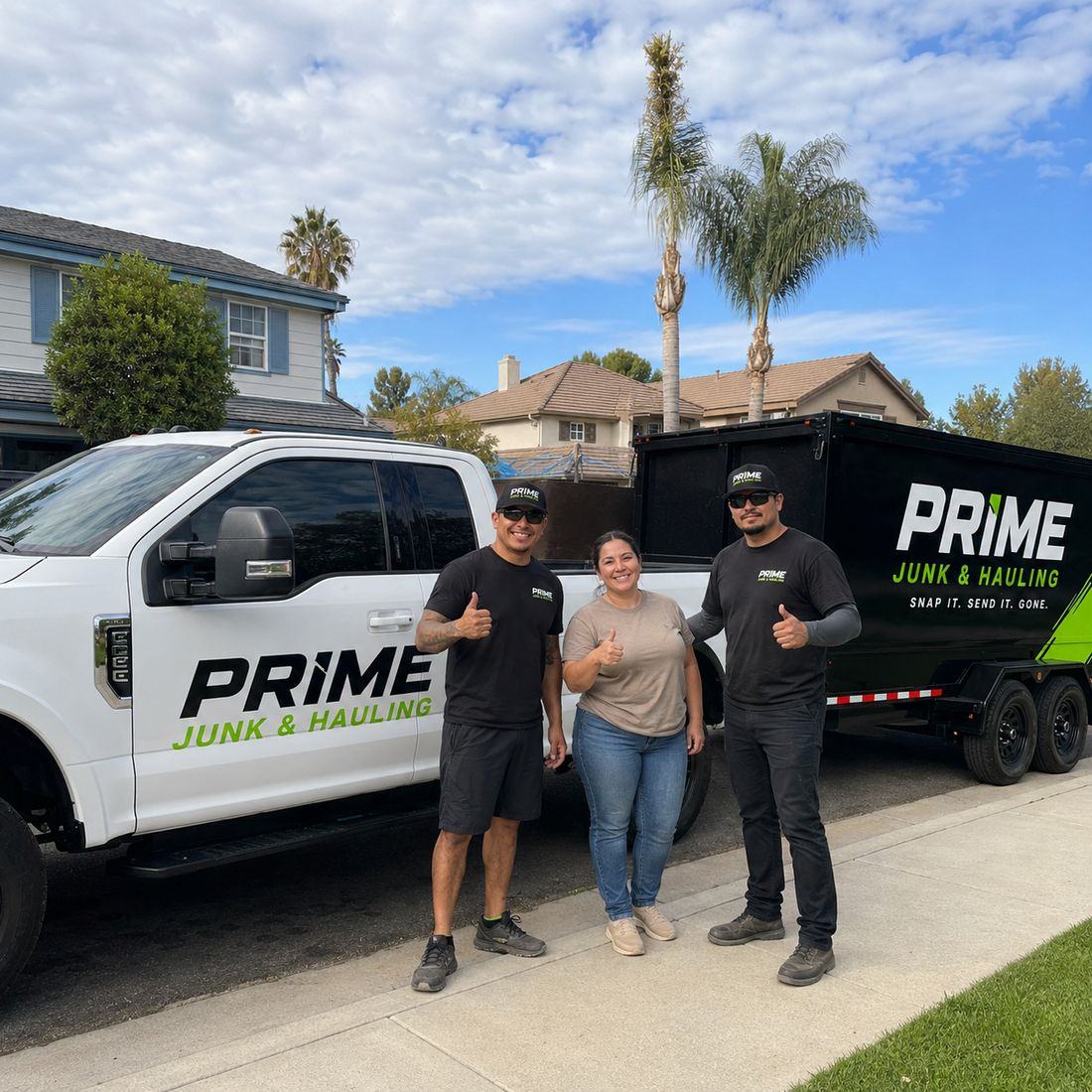 A happy Prime Junk & Hauling customer giving a thumbs up with two uniformed crew members in front of the branded truck and trailer